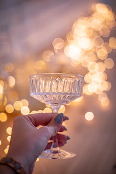 A crystal glass held by a hand with festive bokeh lighting in the background, creating an elegant, celebratory mood.