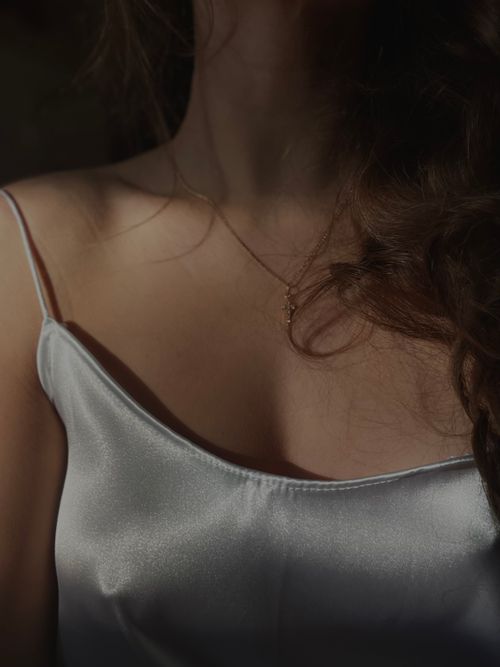 Free Close-up of a woman's neckline wearing a white satin top with delicate lighting. Stock Photo