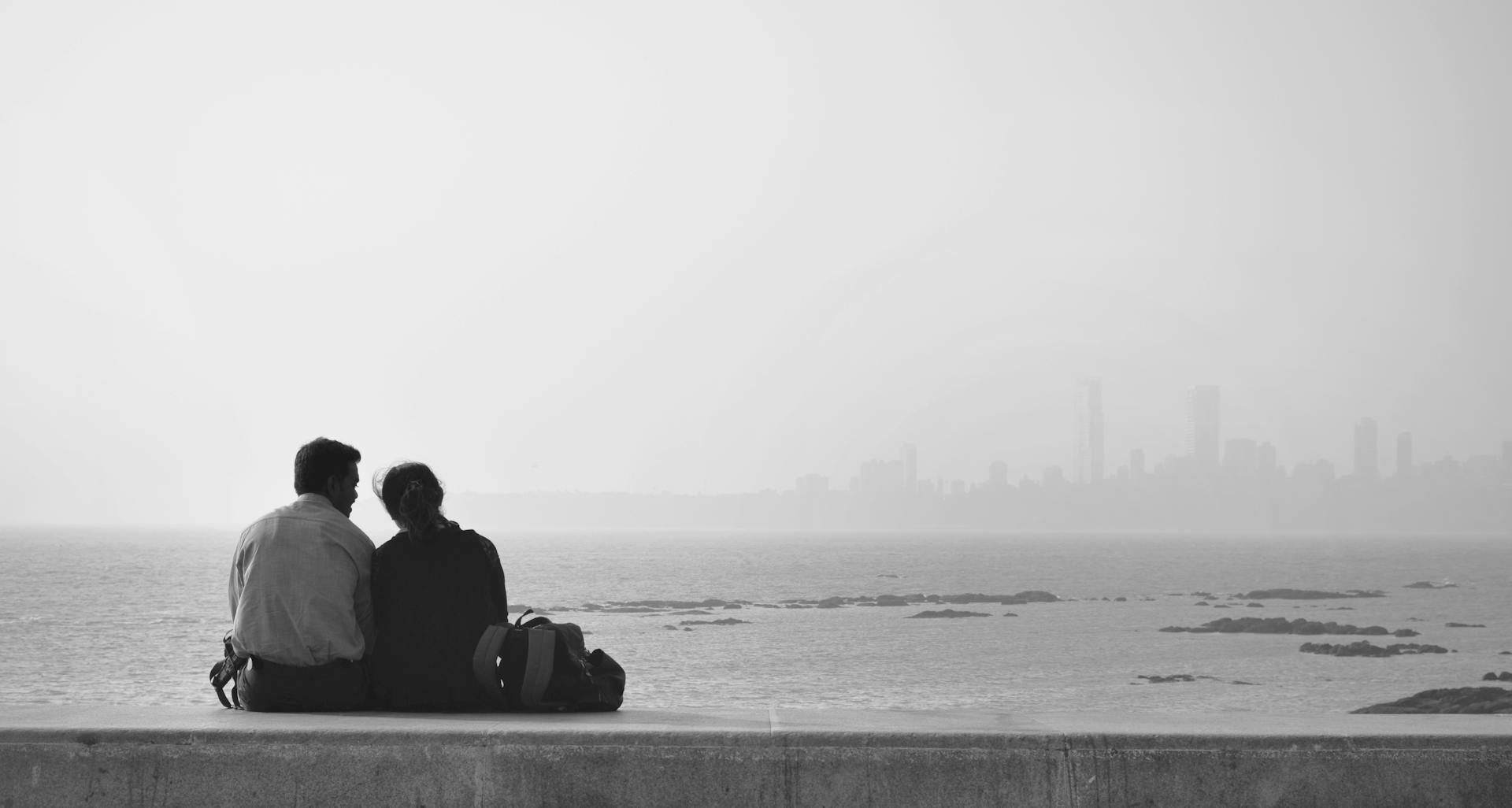 A couple enjoys the serene sea view with Mumbai skyline in the background, a moment of tranquility and connection.