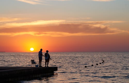 Silhouette of Two People Standing on Dock and Fishing during Sunset