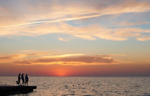 Free Silhouette of Three People Standing on Dock and Fishing during Sunset Stock Photo