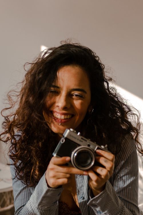 Free Portrait of a cheerful woman holding a vintage camera, capturing a joyful moment. Stock Photo