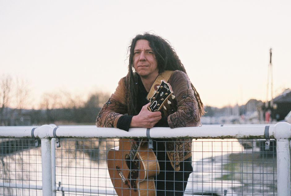 Man with dreadlocks holding acoustic guitar by the canal in Inverness, Scotland.