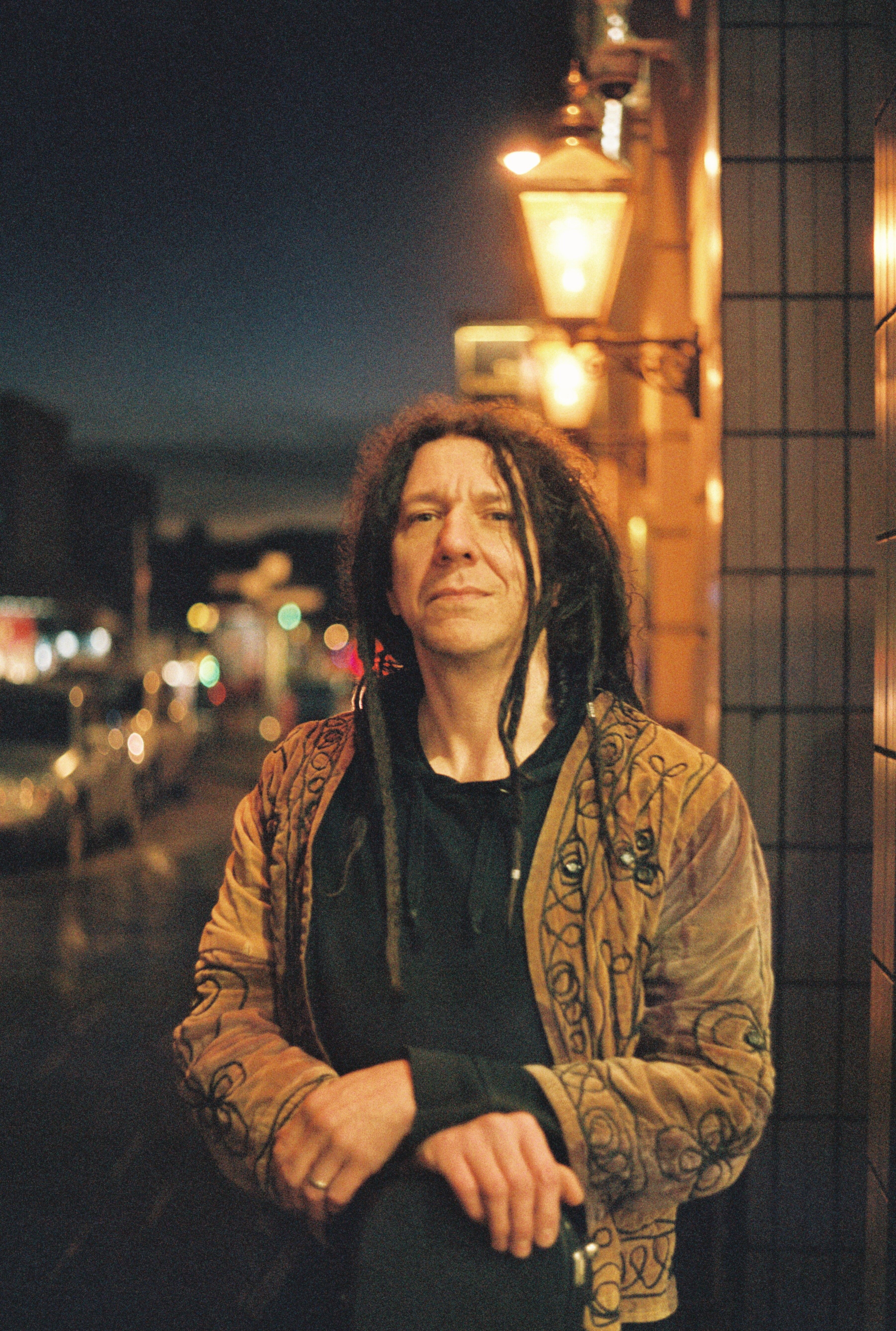 Nighttime street portrait of a man with dreadlocks in Inverness, showcasing urban style and mood lighting.