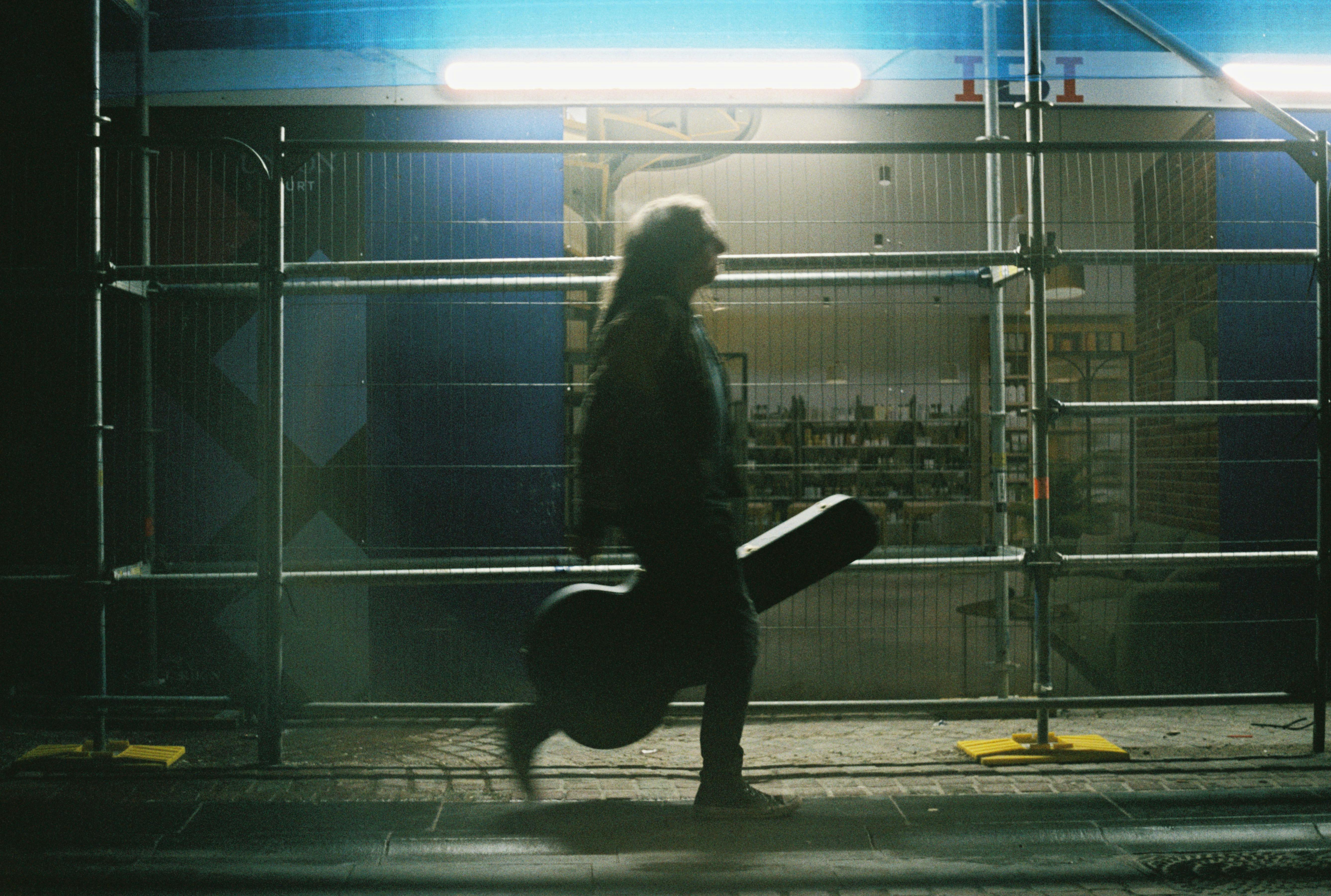 A musician carrying a guitar case walks past a construction site at night in Inverness, Scotland.