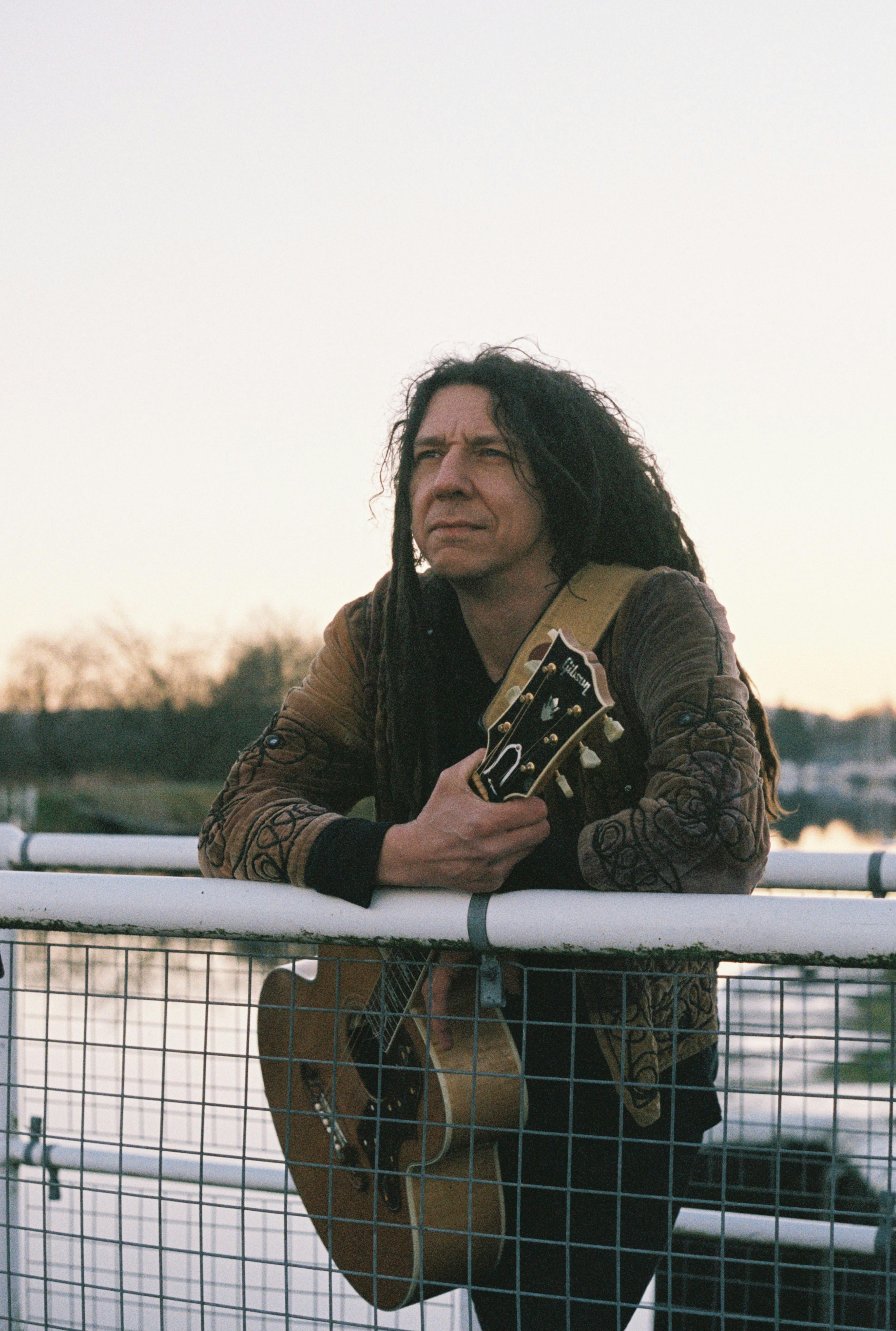 Musician enjoying a serene moment with guitar by a river in Inverness, Scotland.