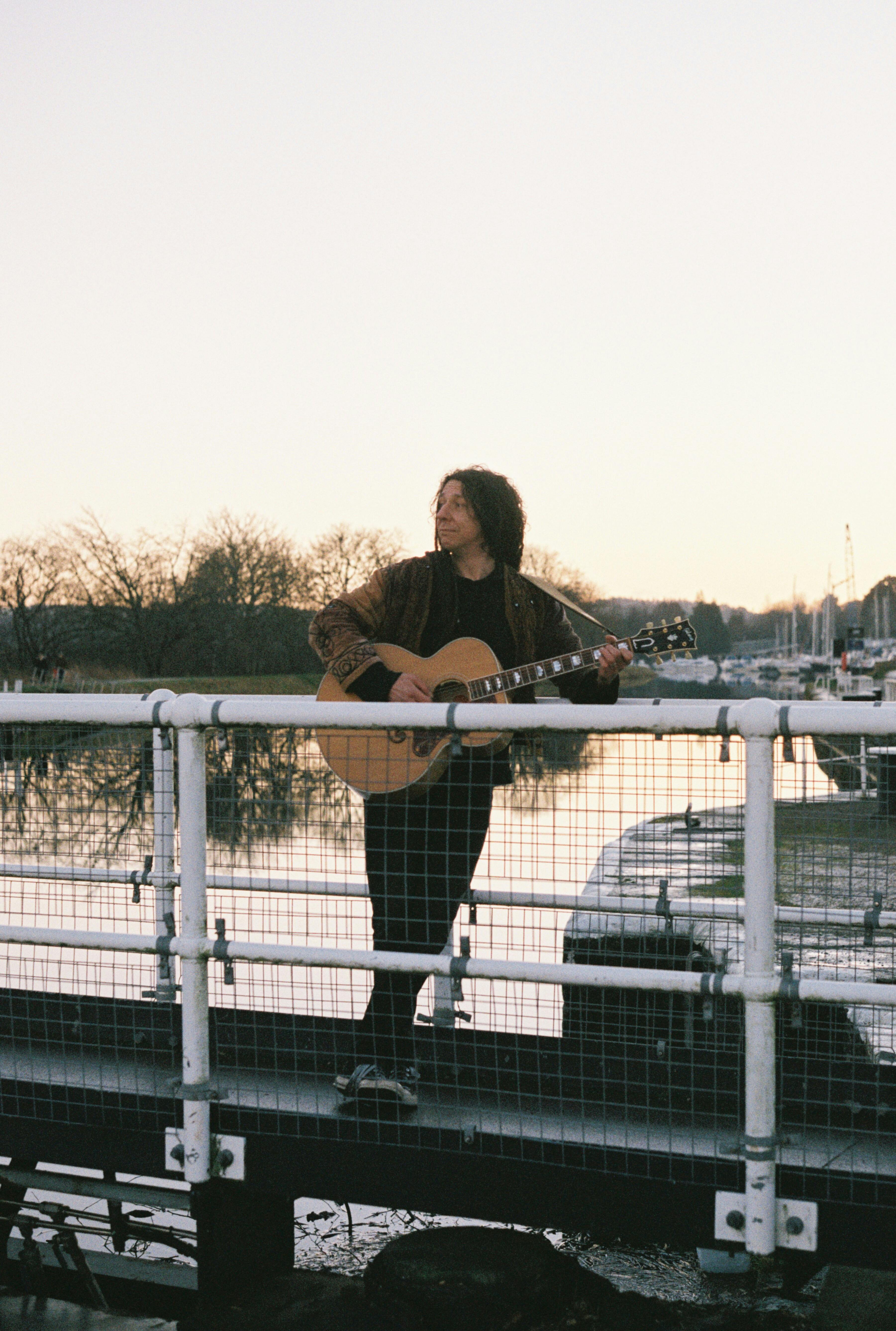 Man playing acoustic guitar on a bridge in Inverness, Scotland during twilight.
