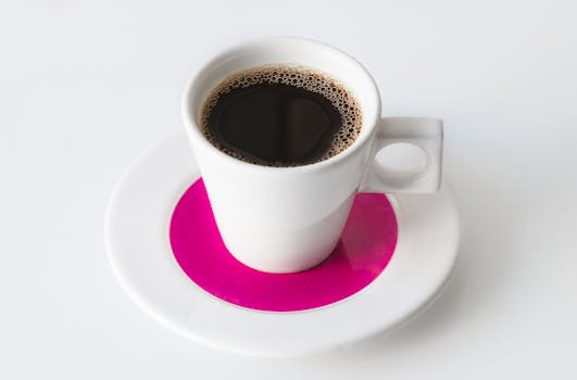Close-up of a steaming black coffee in a stylish white cup on a saucer with a vibrant pink accent.