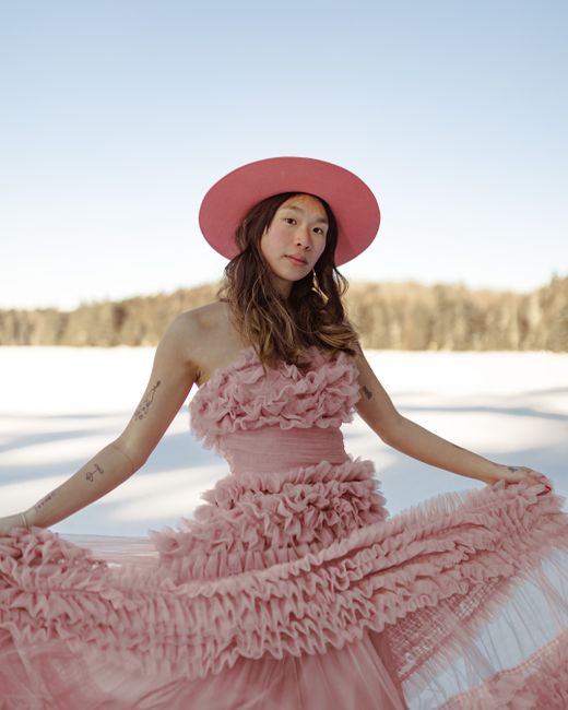 A woman in a pink dress and hat poses artistically against a snowy winter backdrop.