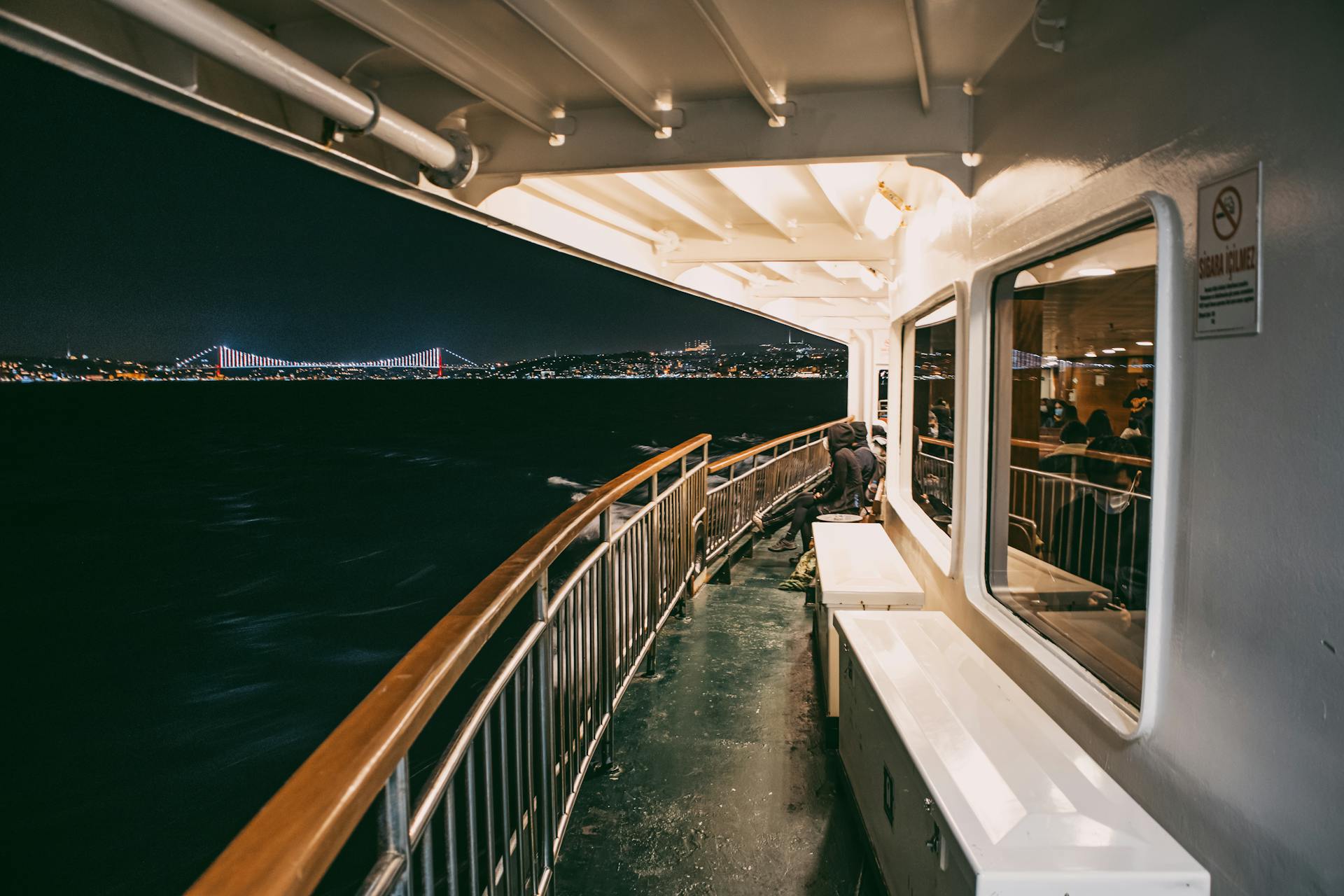 Experience a vibrant night ferry journey with city lights over Istanbul's Bosphorus Bridge.