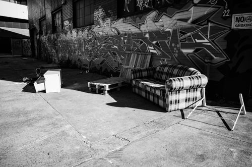Free Black and white photo of an urban alley with graffiti and abandoned furniture including a sofa and chair. Stock Photo