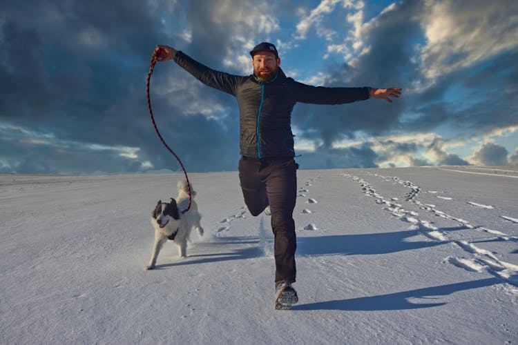 A Man Running In The Snow With His Dog 