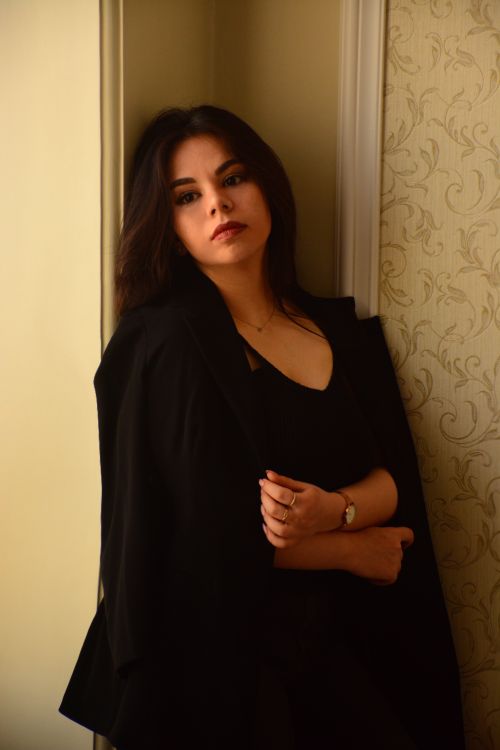 Free Stylish woman in black clothing leaning against a wall indoors, showcasing elegance. Stock Photo
