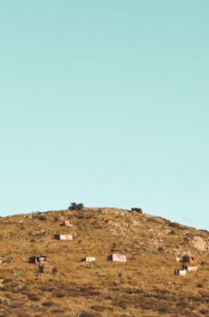Isolated shacks on an arid hill under a bright blue sky, capturing rural simplicity.