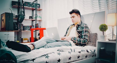 使用银色macbook坐在床上的绿色，蓝色和黑色格子运动衫的男人