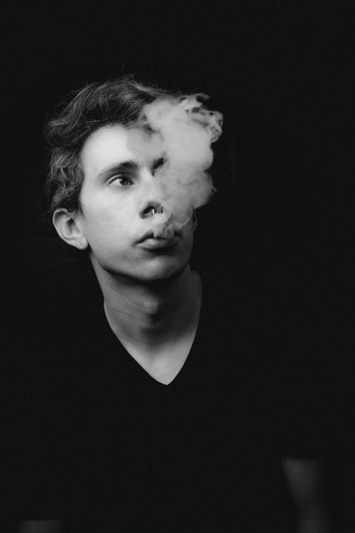 Free Artistic black and white portrait of a man exhaling smoke against a dark background. Stock Photo