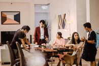 Young professionals engaging in a casual office meeting, wearing masks and discussing in a modern setting.