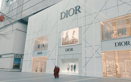 Free Elegant Dior storefront against urban backdrop featuring window displays and shoppers. Stock Photo
