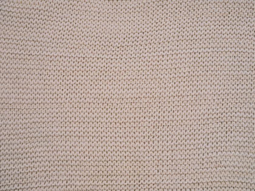Macro close-up of a beige knitted fabric face, fine even rows of loops filling the frame.