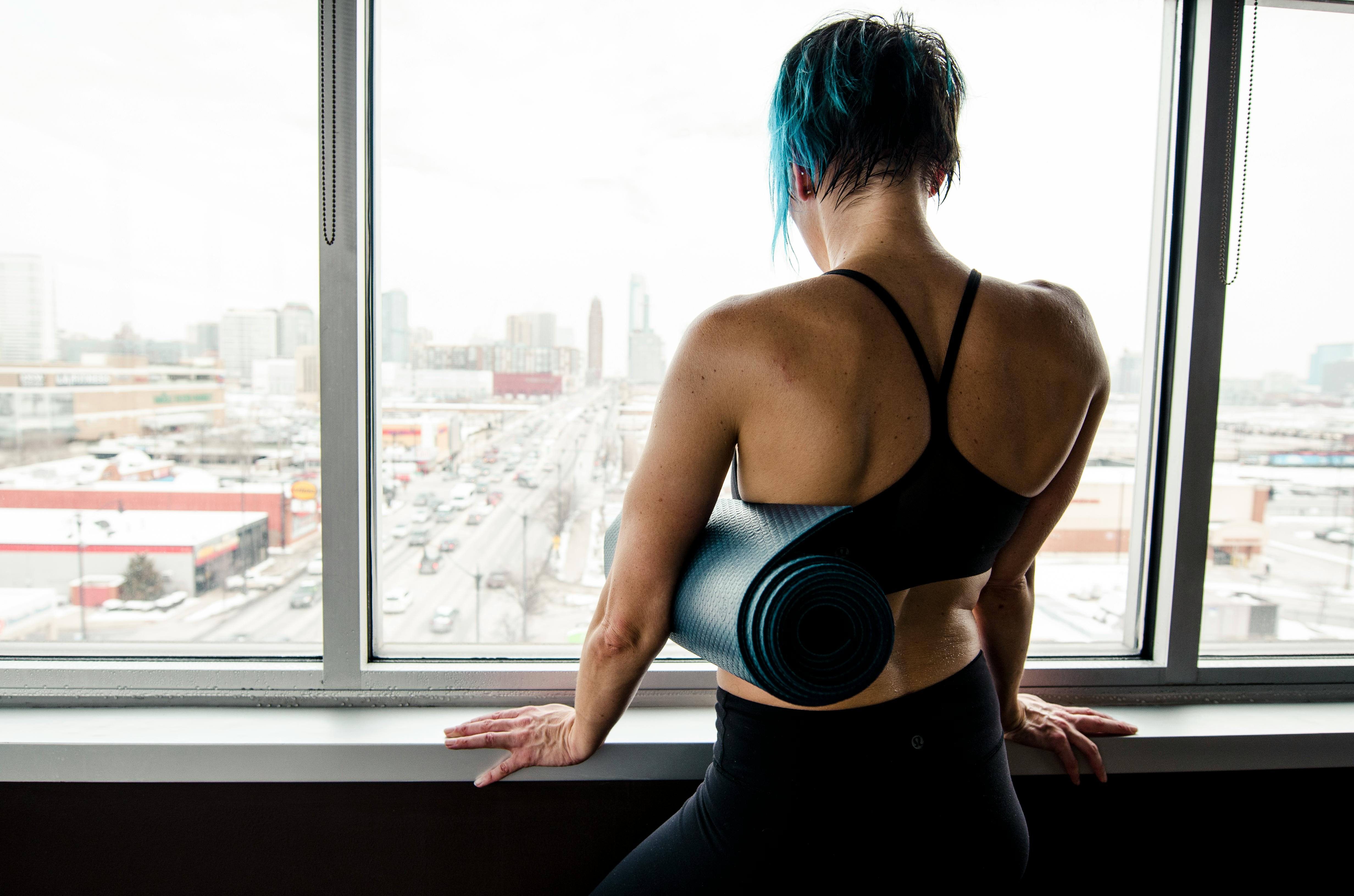 woman in black top holding yoga mat while looking at the window