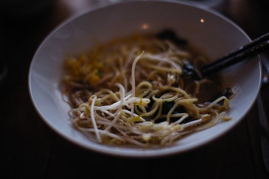 Close-up of a delicious noodle soup with bean sprouts in a ceramic bowl, served with chopsticks.