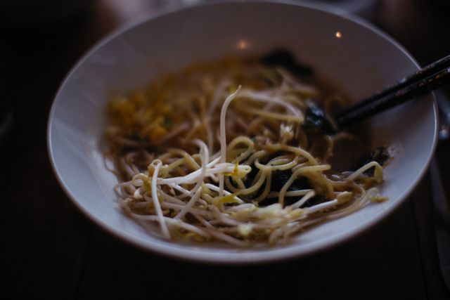 Close-up of a delicious noodle soup with bean sprouts in a ceramic bowl, served with chopsticks.