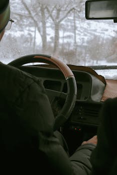 Man driving through a winter landscape with snow outside, focusing on steering wheel perspective.
