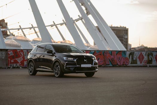 Stylish black car parked in an urban setting with graffiti and modern architecture at sunset.