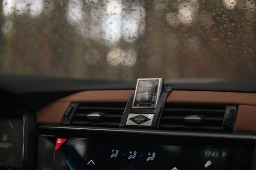 Close-up of a car dashboard showing a clock and controls with raindrops on the window.