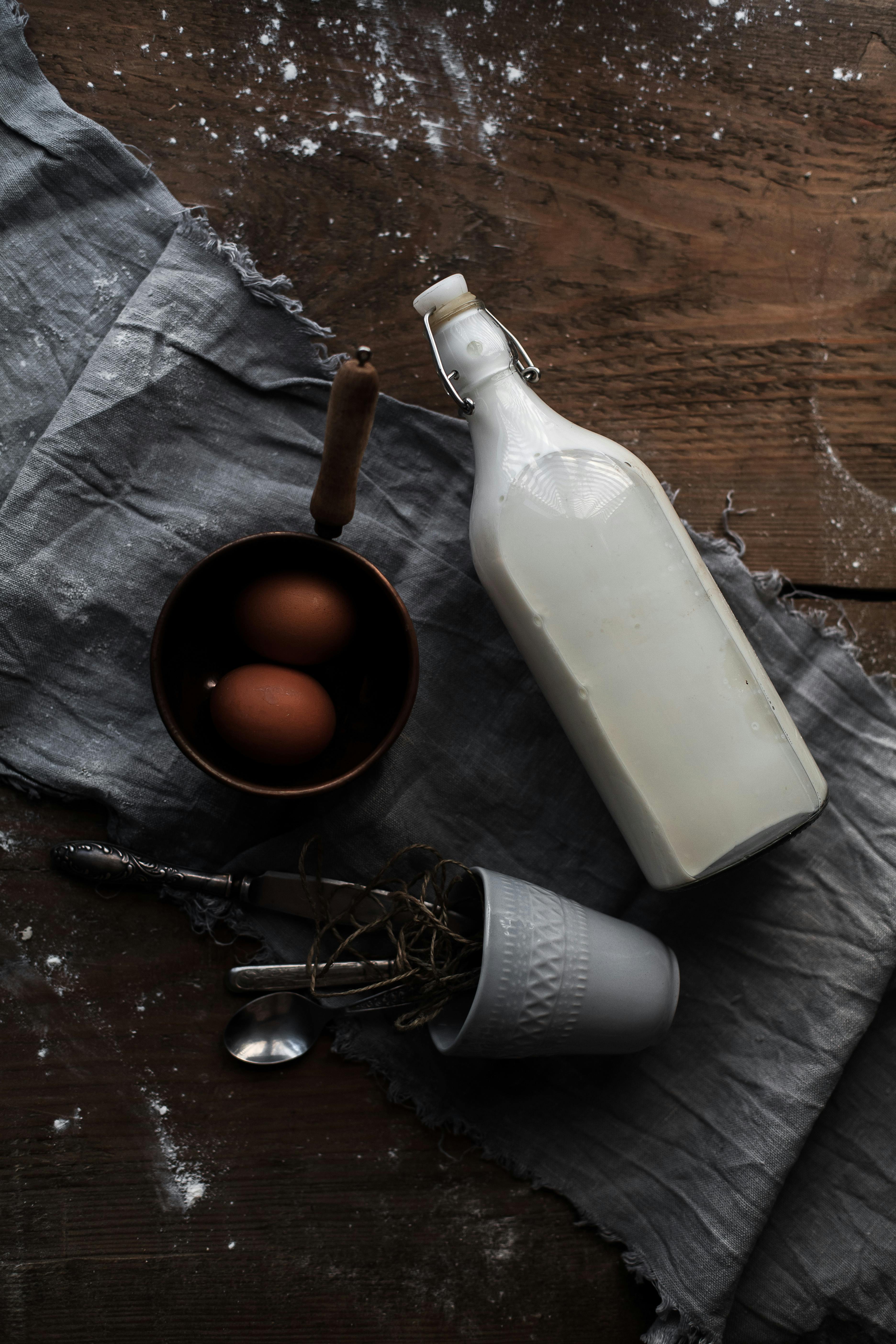 Flat lay image showing eggs, milk bottle, and utensils on a textured cloth for rustic kitchen themes.