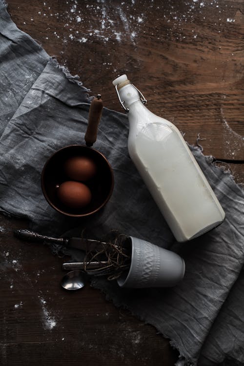 Free Bottle of Milk and Saucepan with Eggs next to Cup with Cutlery Stock Photo
