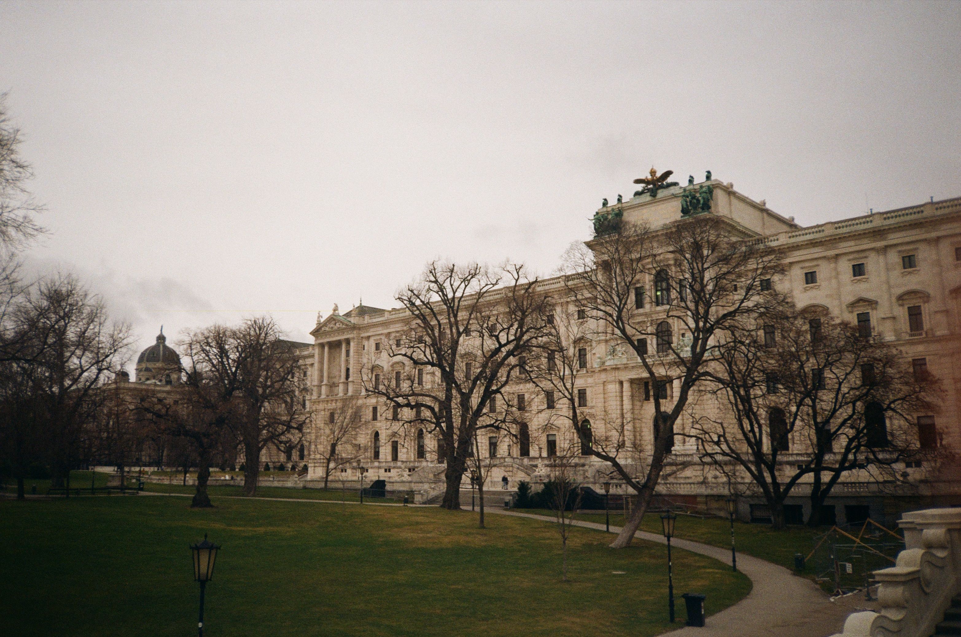 Elegant historical building in Vienna surrounded by leafless trees and paved pathways.