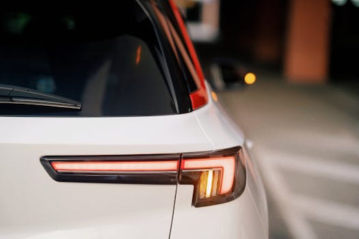 Detailed rear view of a car taillight with red and amber lights in a parking lot.