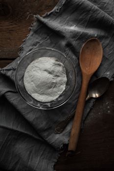 A rustic kitchen flat lay with a glass bowl of flour, wooden spoon, and cloth.