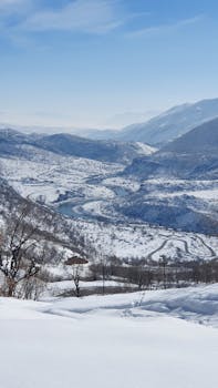 Explore a stunning winter scene with snow-covered mountains, a winding river, and a clear blue sky.