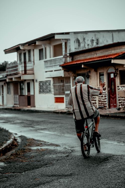 Free An elderly man riding a bike on a wet street in Panama, capturing a sense of freedom and nostalgia. Stock Photo