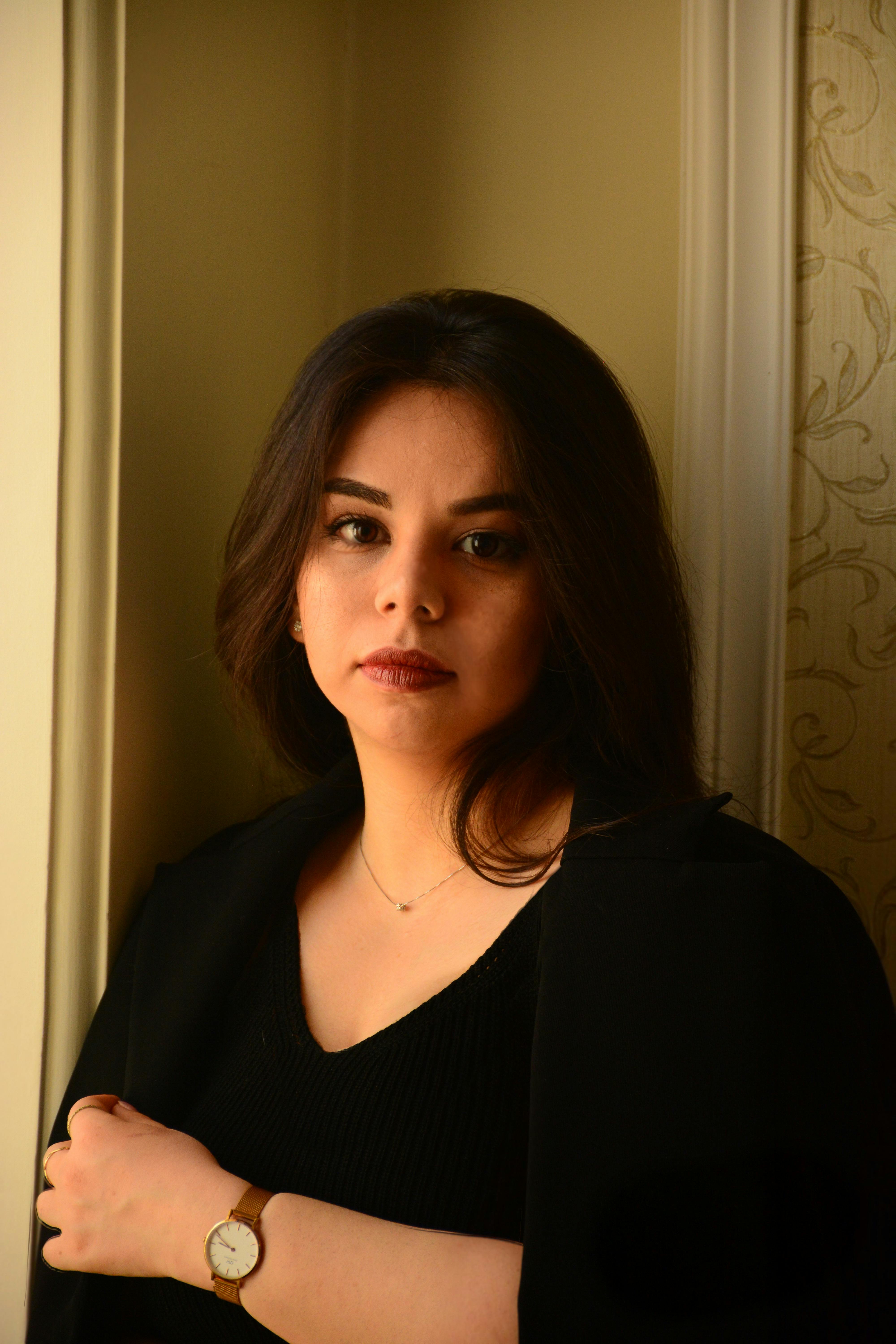 Portrait of a woman in a black shirt standing by a window, elegant and thoughtful.