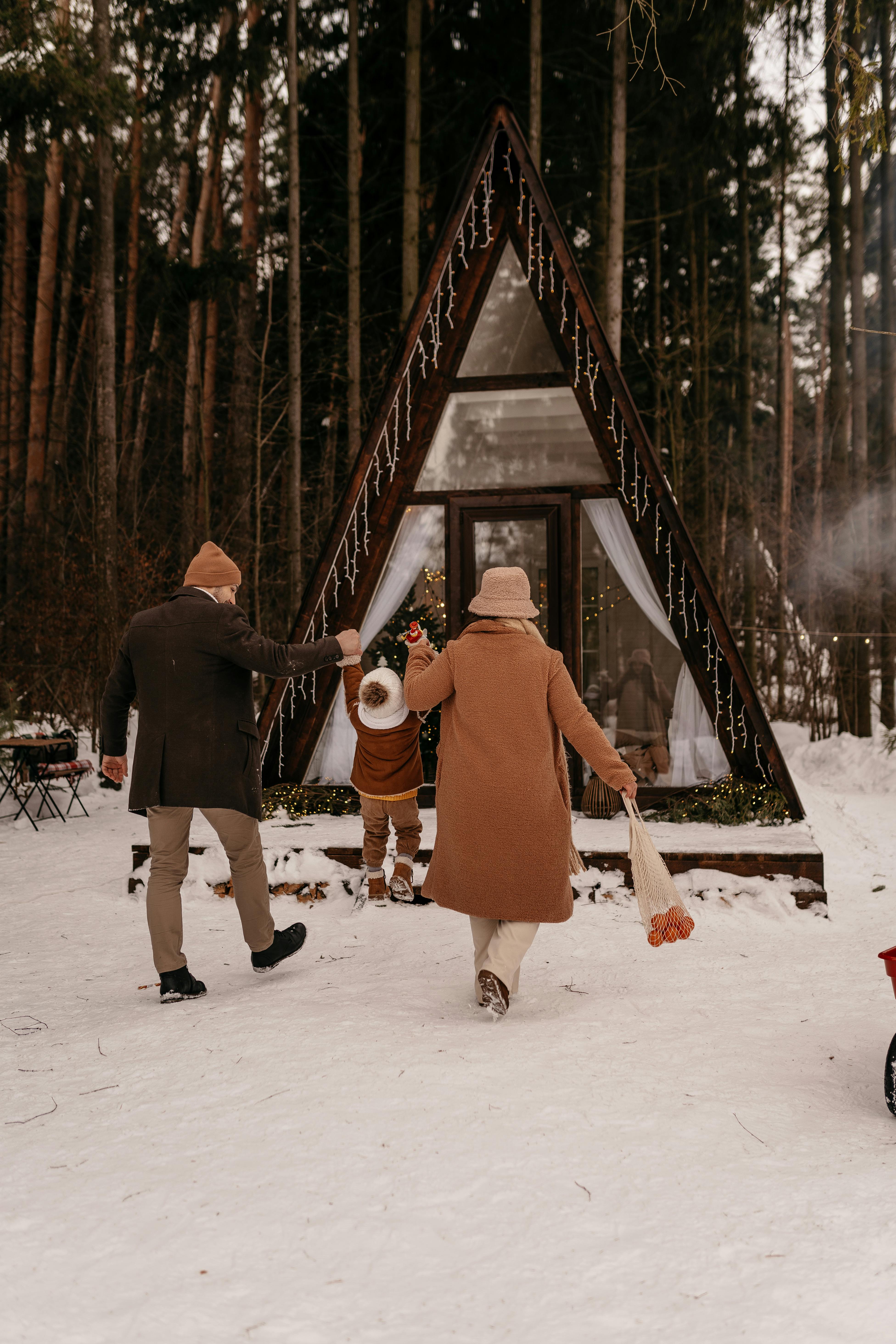 Family walking to an A-frame cabin in a snowy forest. Warm clothes and holiday mood.