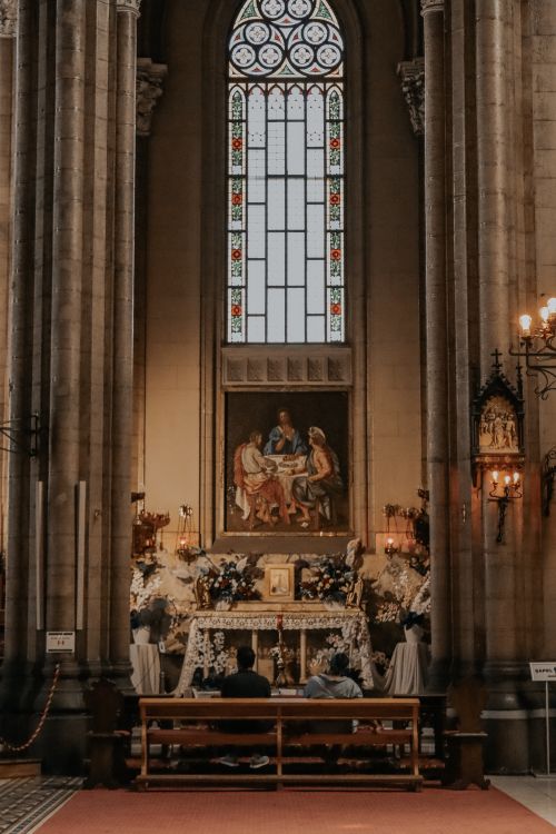Free A serene view of an ornate church interior featuring a stained glass window and people sitting in pews. Stock Photo
