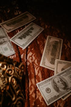 US dollar bills artfully placed on ornate lace fabric with warm, luxurious tones.
