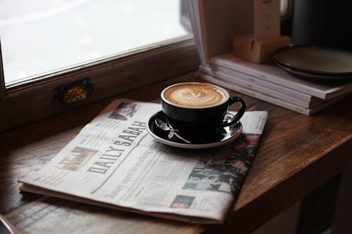 Black Ceramic Cup of Latte  Art on Newspaper