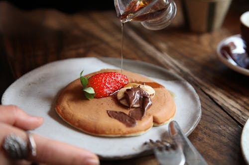 A Close-Up Shot of a Person Pouring Syrup on a Pancake