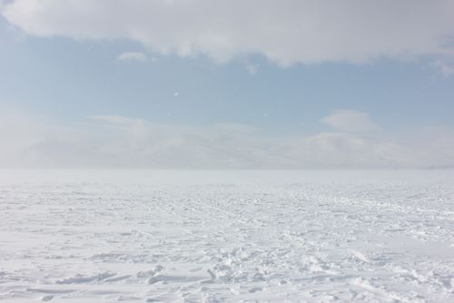 Free A vast snow-covered lake surrounded by misty mountains under a clear blue sky. Stock Photo