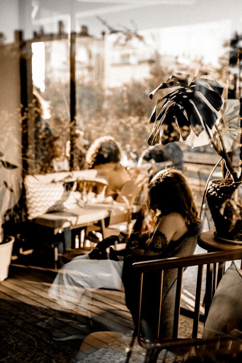 Free Warm-toned café interior featuring people, reflections, and potted plants, perfect for lifestyle and design themes. Stock Photo