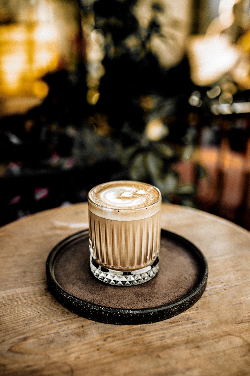 elegant latte art in a glass cup on a rustic wooden table, indoor cafe setting.