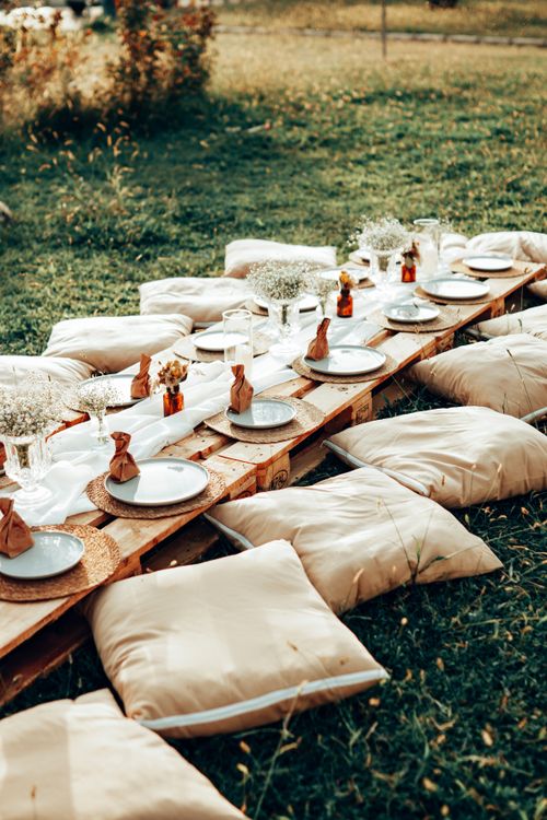 Free Charming outdoor picnic setup with cushions and rustic wooden pallets in a grassy field. Stock Photo