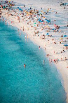 Aerial shot of a crowded beach with white sand and turquoise water under a sunny sky.