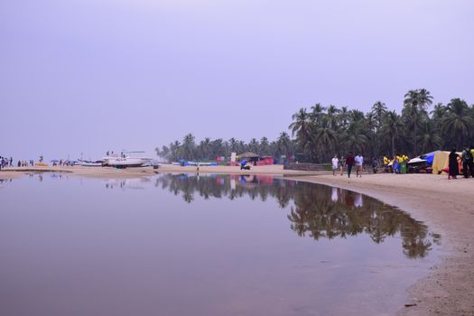 Serene beach scene with reflections of boats and palm trees, people enjoying a tropical setting.