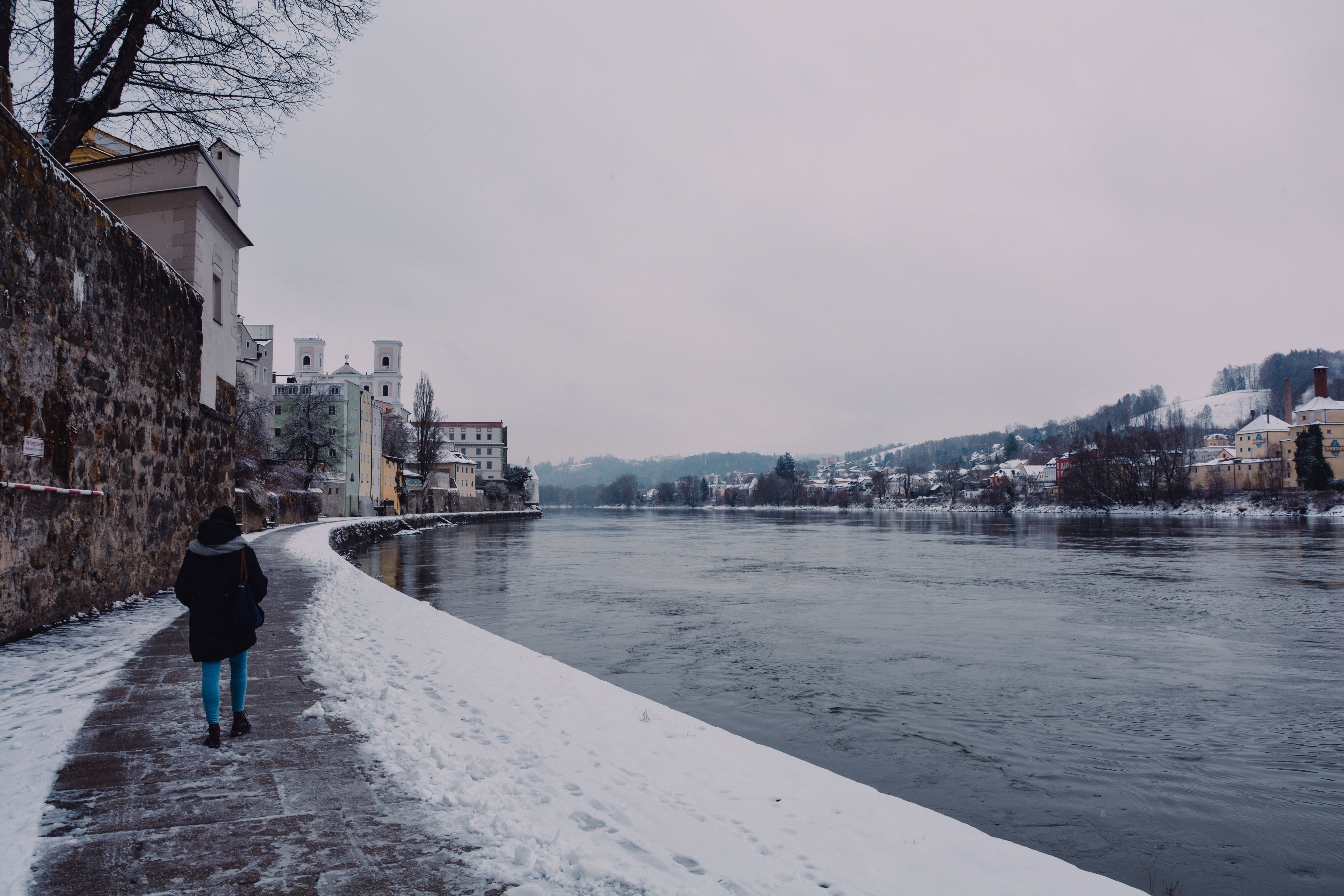 A peaceful riverside walk in snowy Passau, showcasing winter scenery and historical architecture.