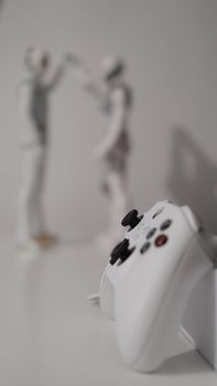 Close-up of a white gaming controller with blurred humanoid figures in the background.